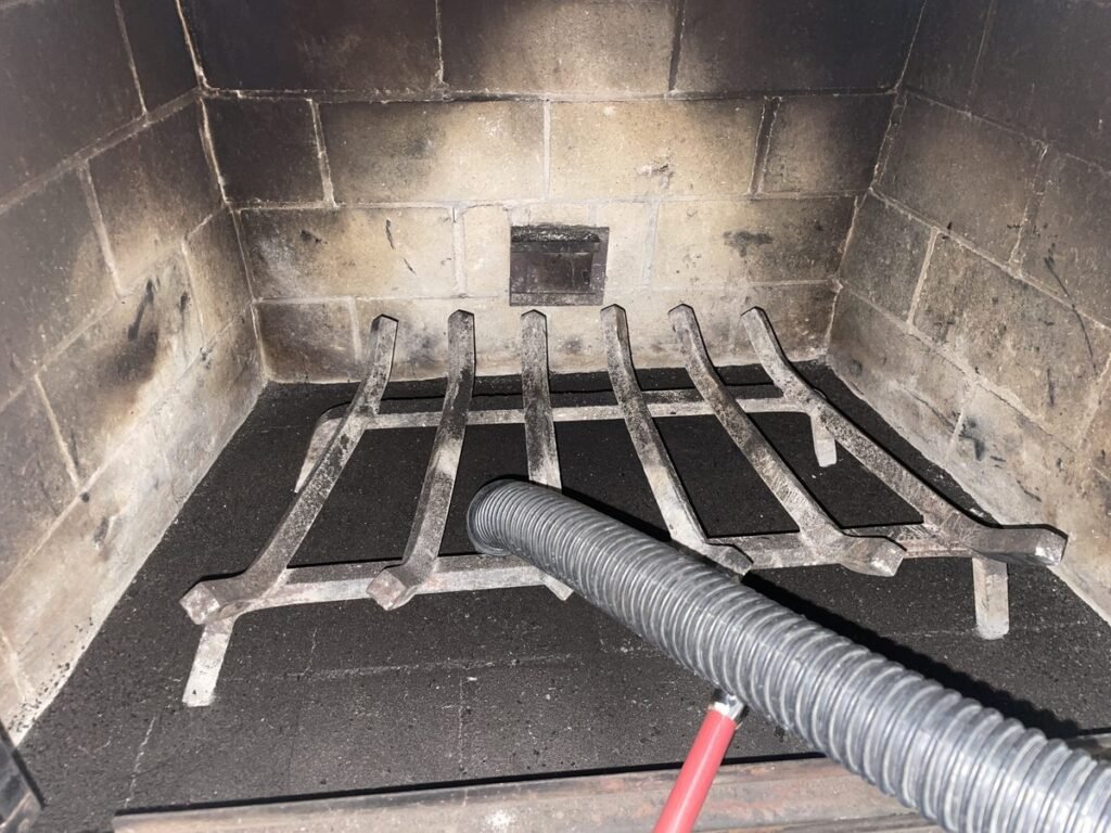 Vacuum hose clearing soot from a fireplace firebox and grate during an ABD chimney cleaning