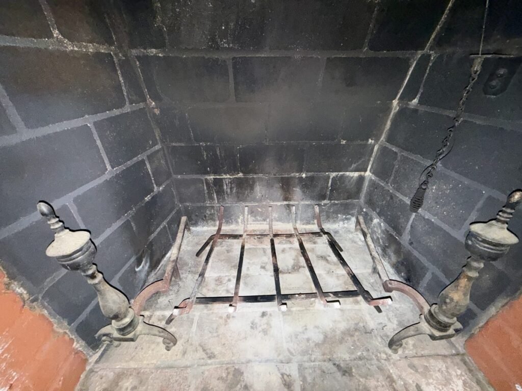 Clean firebox of a wood-burning fireplace with a grate and brass andirons on an ABD chimney cleaning job