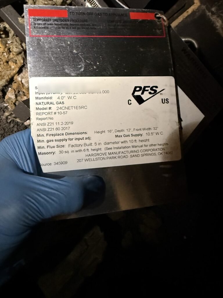 Technician in a blue glove holding a gas log set rating plate during an ABD gas fireplace inspection
